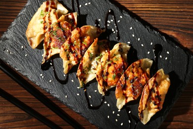 Photo of Tasty fried gyoza (dumplings) and chopsticks on wooden table, top view