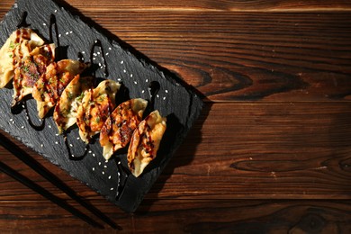 Photo of Tasty fried gyoza (dumplings) and chopsticks on wooden table, top view. Space for text