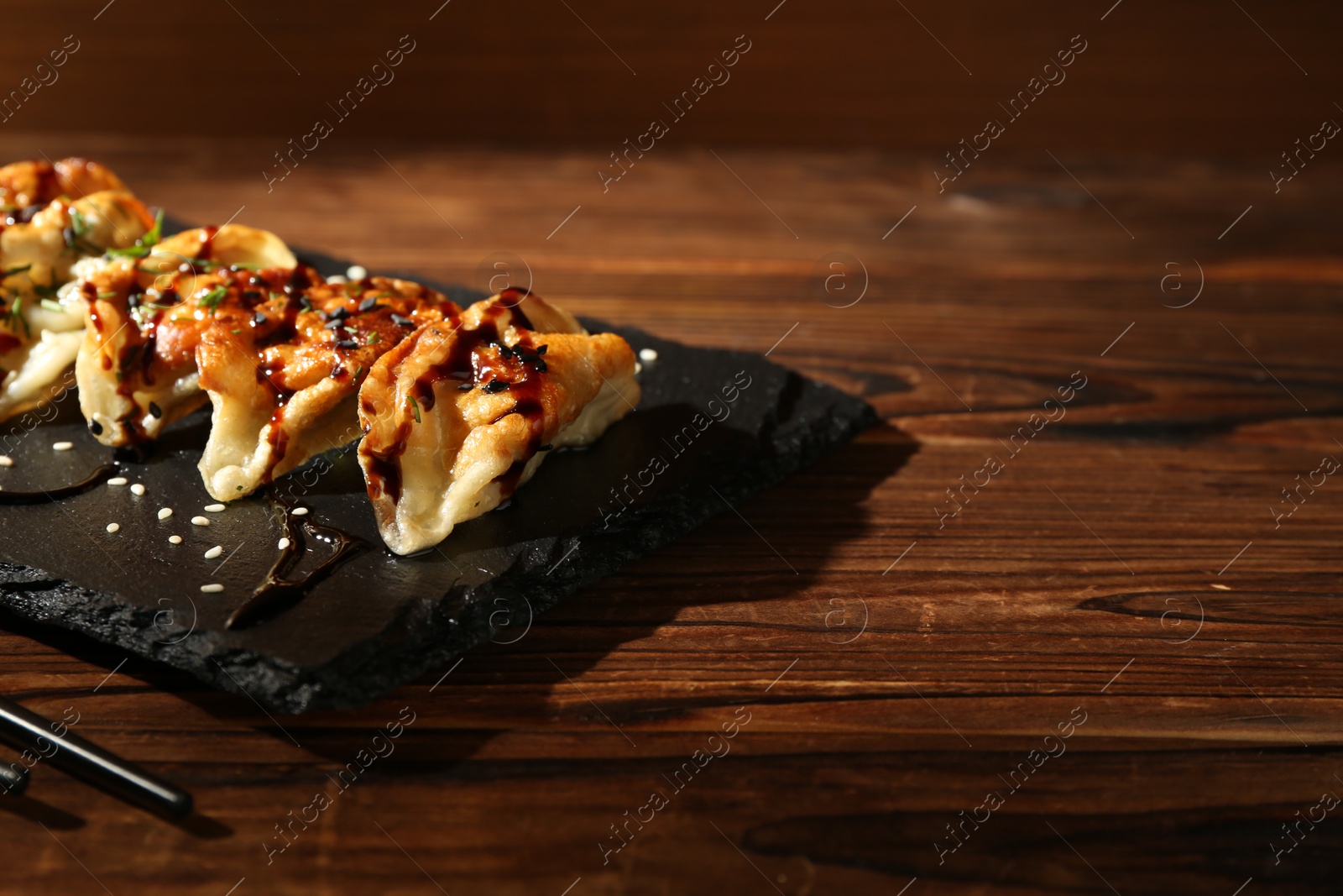 Photo of Tasty fried gyoza (dumplings) and chopsticks on wooden table, closeup. Space for text