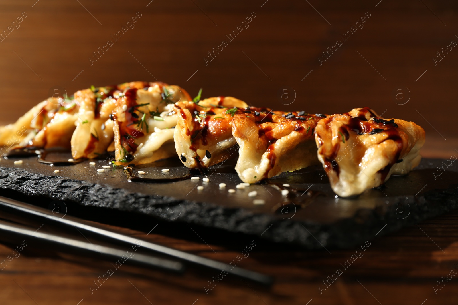 Photo of Tasty fried gyoza (dumplings) and chopsticks on wooden table, closeup