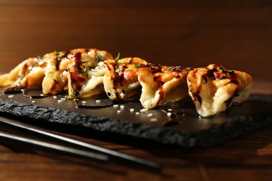 Photo of Tasty fried gyoza (dumplings) and chopsticks on wooden table, closeup