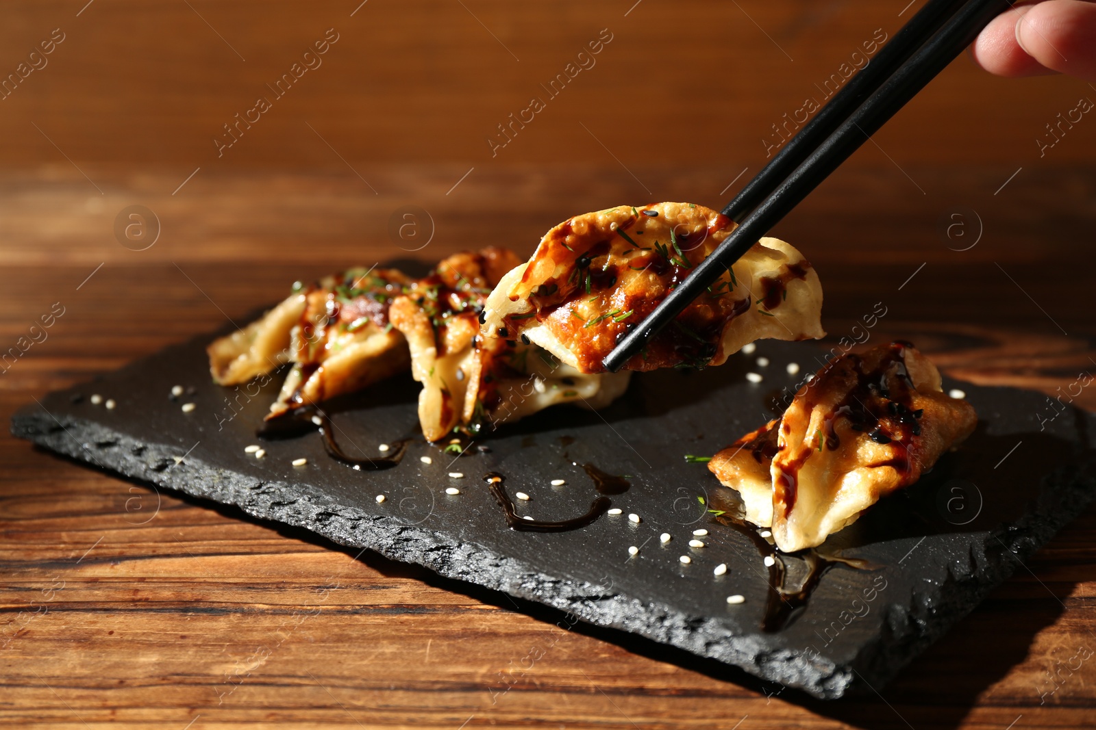 Photo of Woman taking tasty fried gyoza (dumpling) with chopsticks at wooden table, closeup