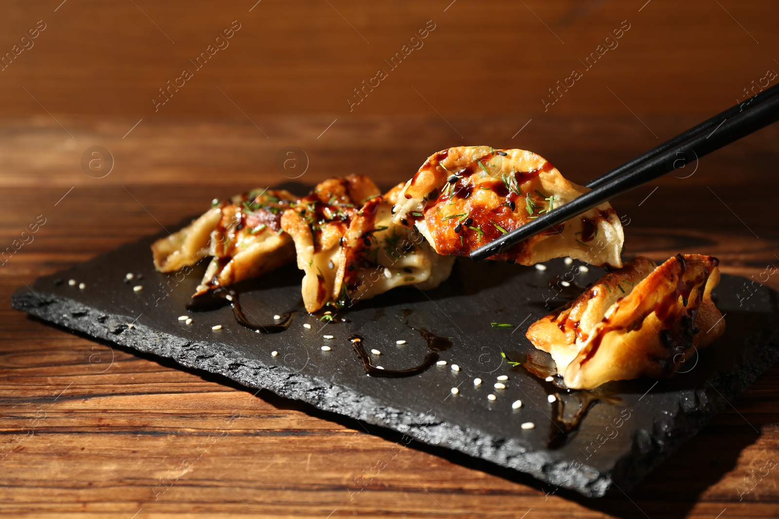 Photo of Taking tasty fried gyoza (dumpling) with chopsticks on wooden table, closeup