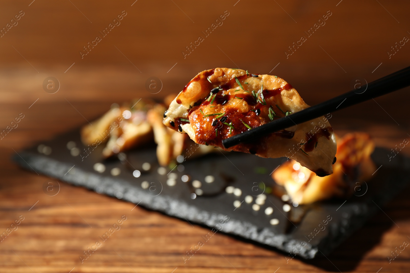 Photo of Taking tasty fried gyoza (dumpling) with chopsticks on wooden table, closeup