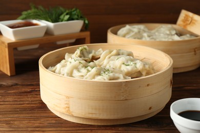 Photo of Tasty boiled gyoza (dumplings) in bamboo steamers on wooden table, closeup