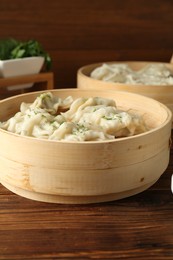 Photo of Tasty boiled gyoza (dumplings) in bamboo steamers on wooden table, closeup