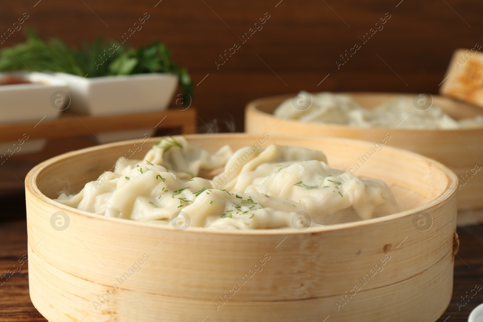 Photo of Tasty boiled gyoza (dumplings) in bamboo steamers on wooden table, closeup