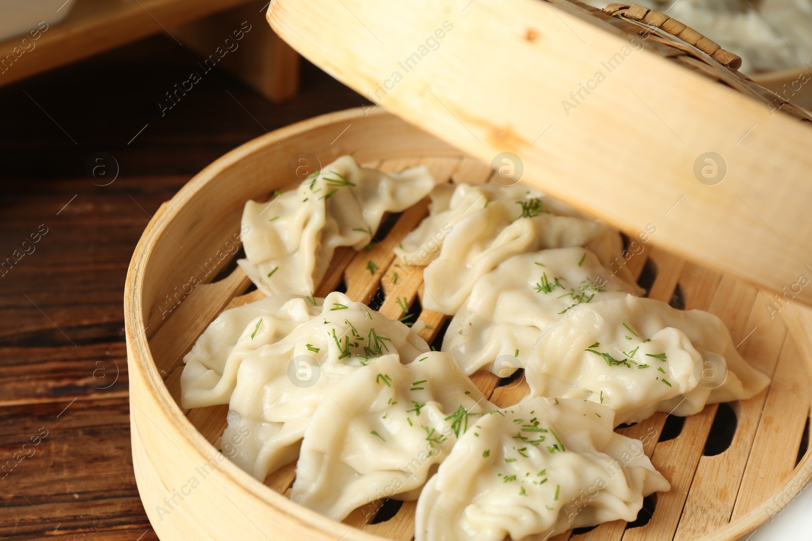 Photo of Tasty boiled gyoza (dumplings) in bamboo steamer on wooden table, closeup