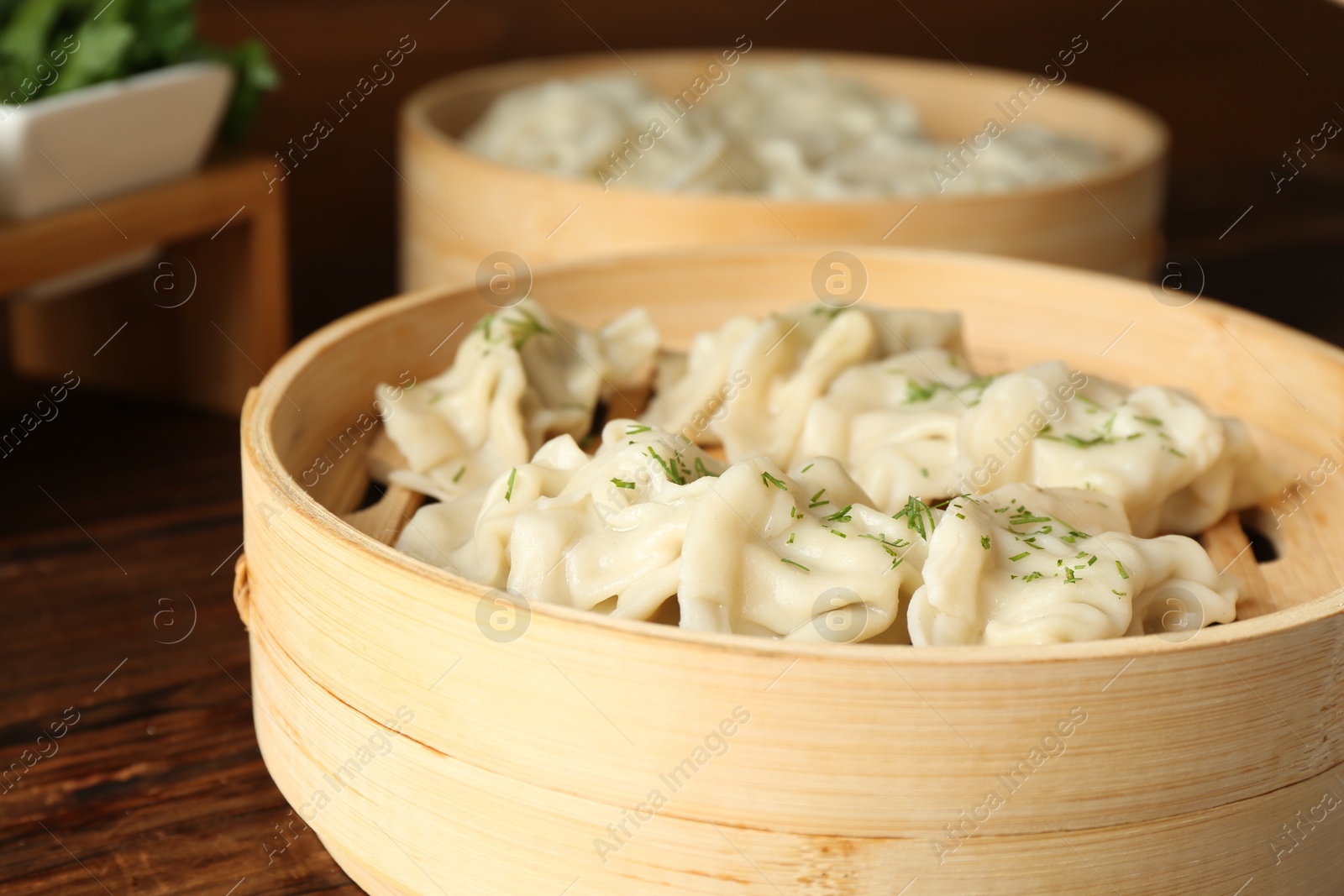 Photo of Tasty boiled gyoza (dumplings) in bamboo steamers on wooden table, closeup