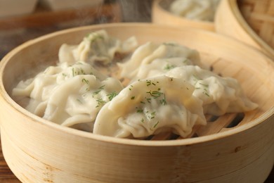 Photo of Tasty boiled gyoza (dumplings) in bamboo steamers on wooden table, closeup