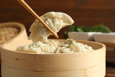 Photo of Taking tasty boiled gyoza (dumpling) with chopsticks on table, closeup