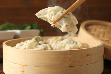 Photo of Taking tasty boiled gyoza (dumpling) with chopsticks on table, closeup