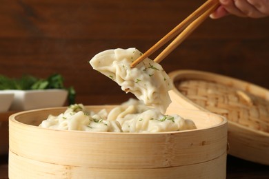 Photo of Taking tasty boiled gyoza (dumpling) with chopsticks on table, closeup