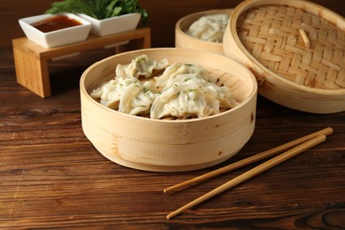 Photo of Tasty boiled gyoza (dumplings) in bamboo steamers and chopsticks on wooden table