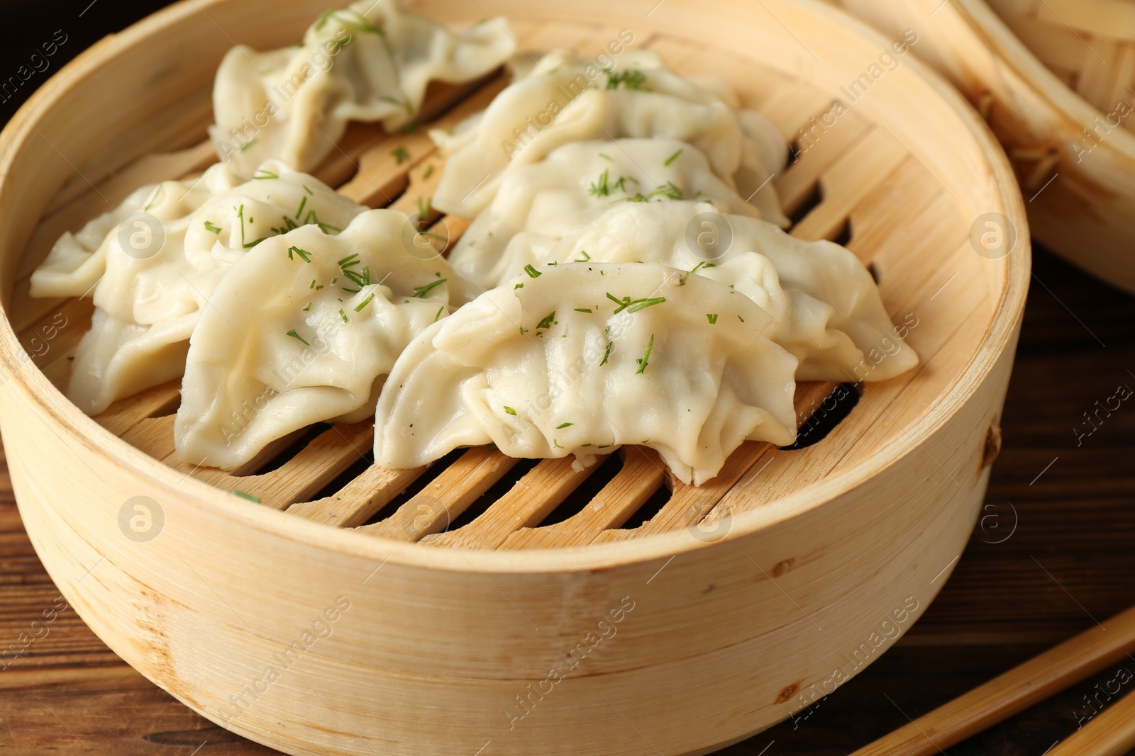 Photo of Tasty boiled gyoza (dumplings) in bamboo steamer and chopsticks on wooden table, closeup