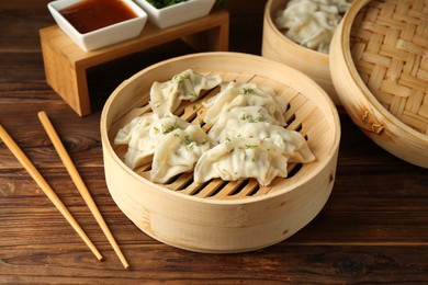 Photo of Tasty boiled gyoza (dumplings) in bamboo steamers and chopsticks on wooden table