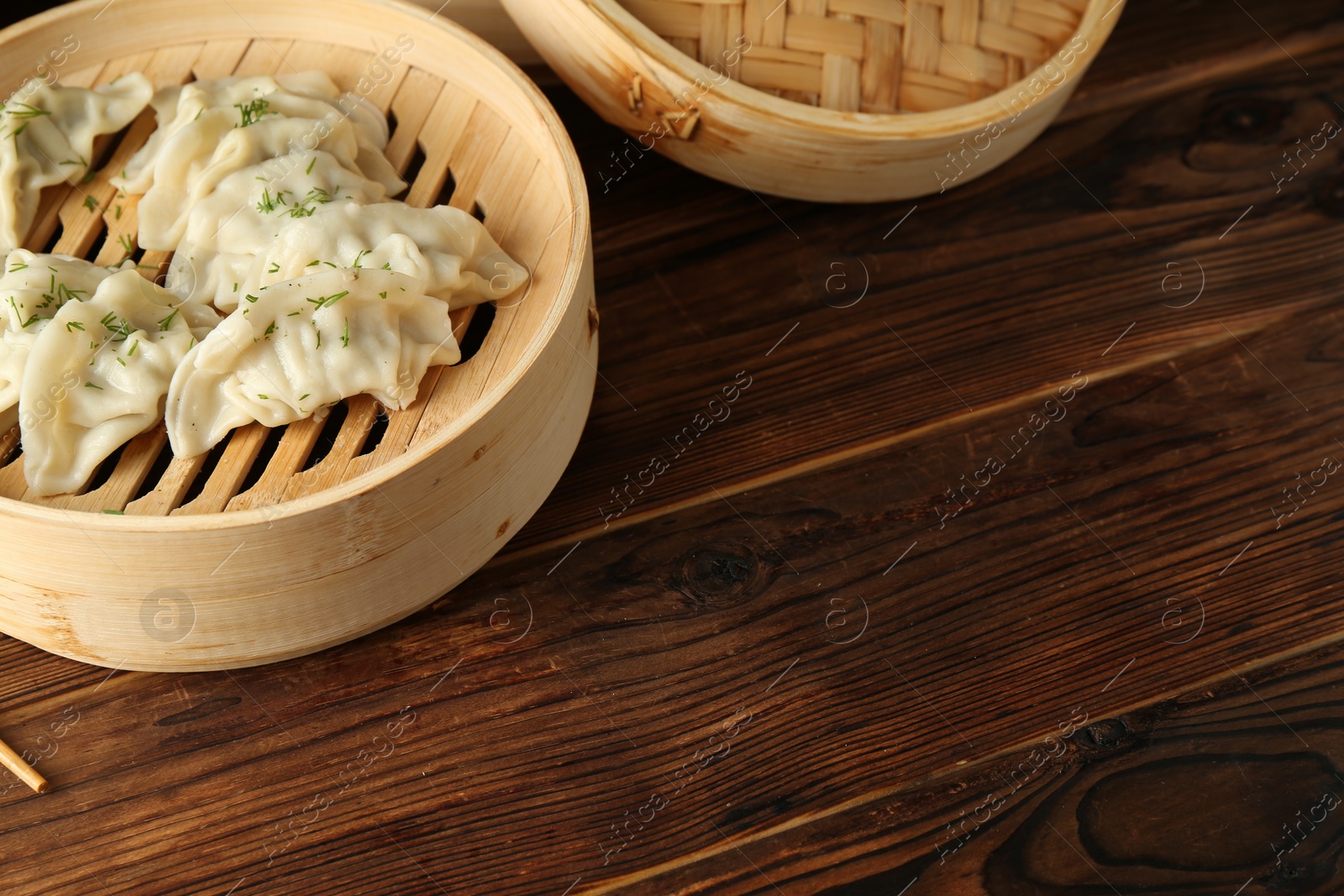 Photo of Tasty boiled gyoza (dumplings) in bamboo steamers on wooden table. Space for text