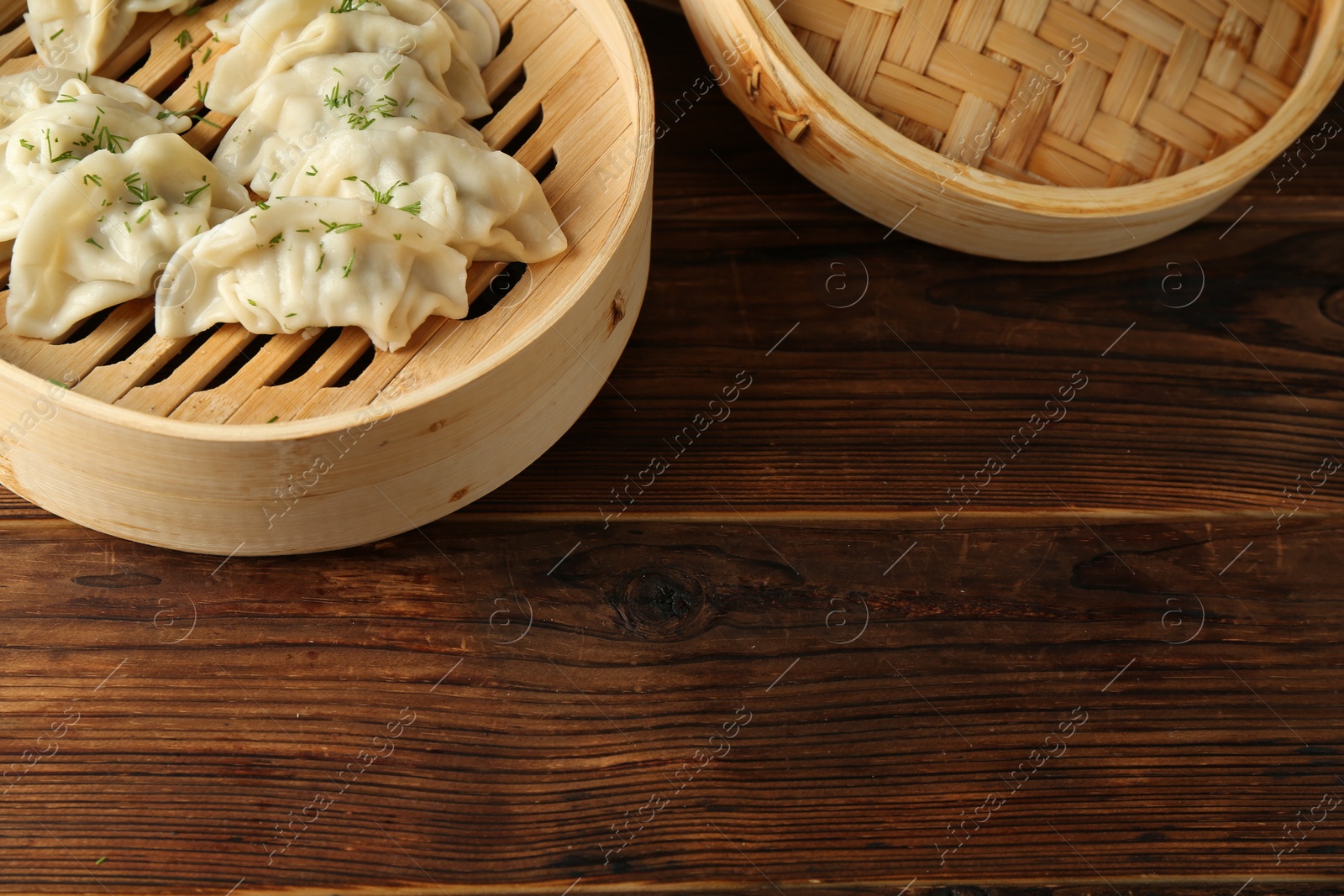 Photo of Tasty boiled gyoza (dumplings) in bamboo steamers on wooden table. Space for text