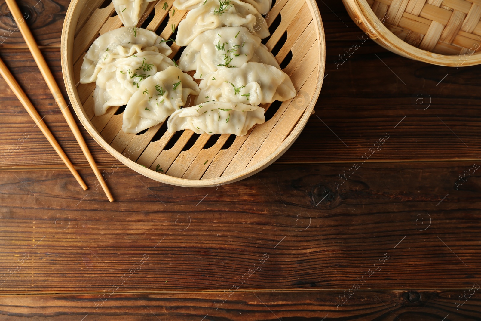 Photo of Tasty boiled gyoza (dumplings) in bamboo steamers and chopsticks on wooden table, flat lay. Space for text