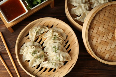 Photo of Tasty boiled gyoza (dumplings) in bamboo steamers, sauce and chopsticks on wooden table, flat lay