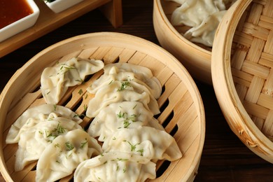 Photo of Tasty boiled gyoza (dumplings) in bamboo steamers on wooden table, closeup