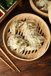 Photo of Tasty boiled gyoza (dumplings) in bamboo steamers, sauce and chopsticks on wooden table, flat lay