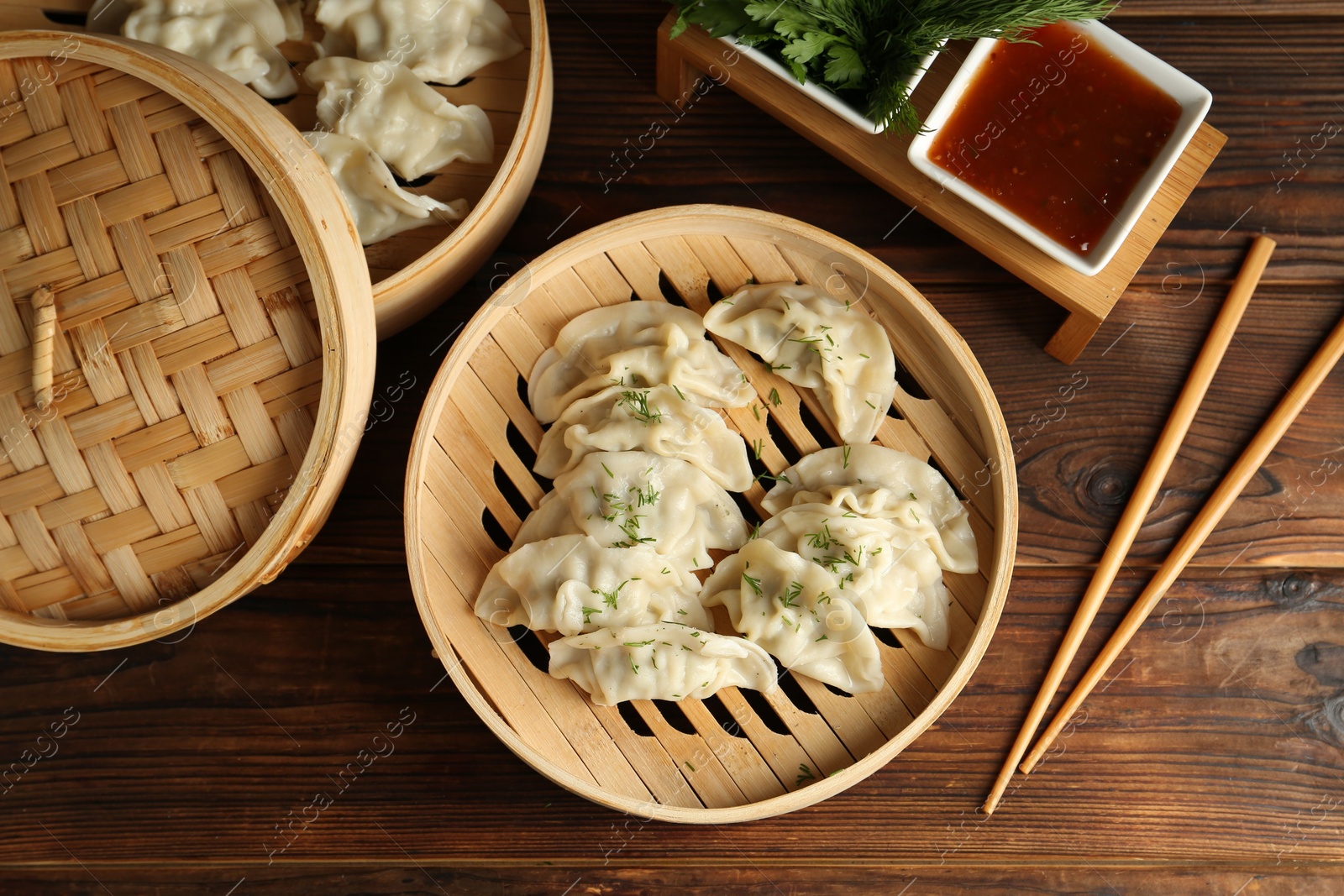 Photo of Tasty boiled gyoza (dumplings) in bamboo steamers, sauce and chopsticks on wooden table, flat lay