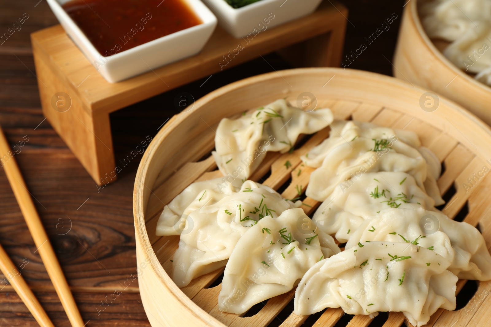 Photo of Tasty boiled gyoza (dumplings) in bamboo steamers, sauce and chopsticks on wooden table, closeup