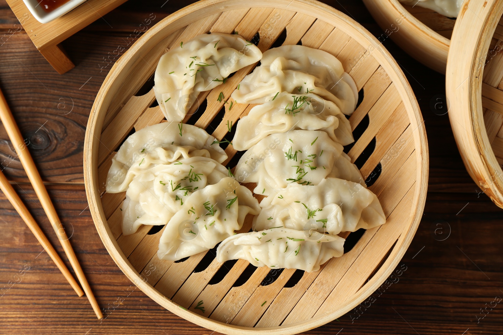 Photo of Tasty boiled gyoza (dumplings) in bamboo steamer and chopsticks on wooden table, flat lay