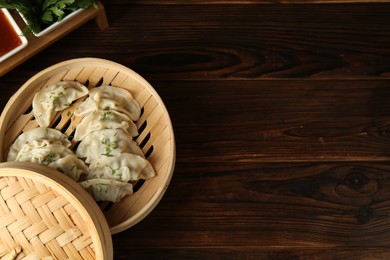 Photo of Tasty boiled gyoza (dumplings) in bamboo steamer on wooden table, flat lay. Space for text