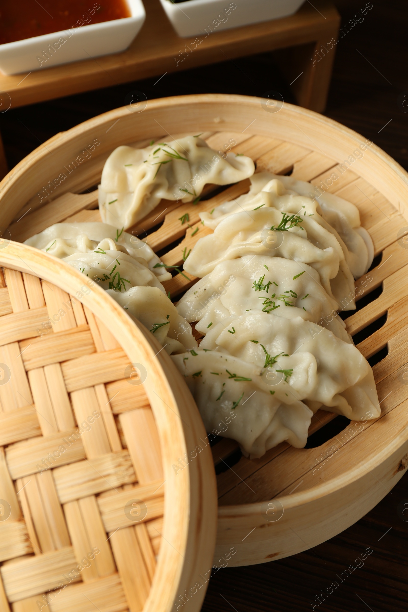 Photo of Tasty boiled gyoza (dumplings) in bamboo steamer on wooden table, closeup