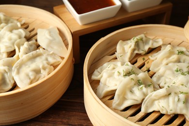 Photo of Tasty boiled gyoza (dumplings) in bamboo steamers, and sauce on wooden table, closeup