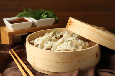 Photo of Tasty boiled gyoza (dumplings) in bamboo steamer and chopsticks on table, closeup