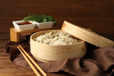 Photo of Tasty boiled gyoza (dumplings) in bamboo steamer and chopsticks on wooden table