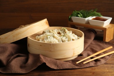 Photo of Tasty boiled gyoza (dumplings) in bamboo steamer and chopsticks on wooden table