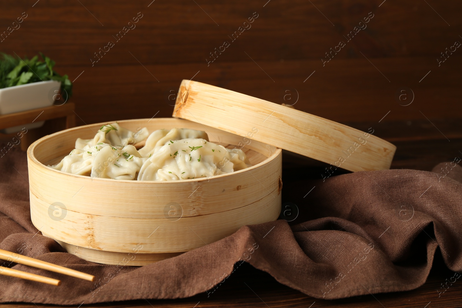 Photo of Tasty boiled gyoza (dumplings) in bamboo steamer and chopsticks on wooden table