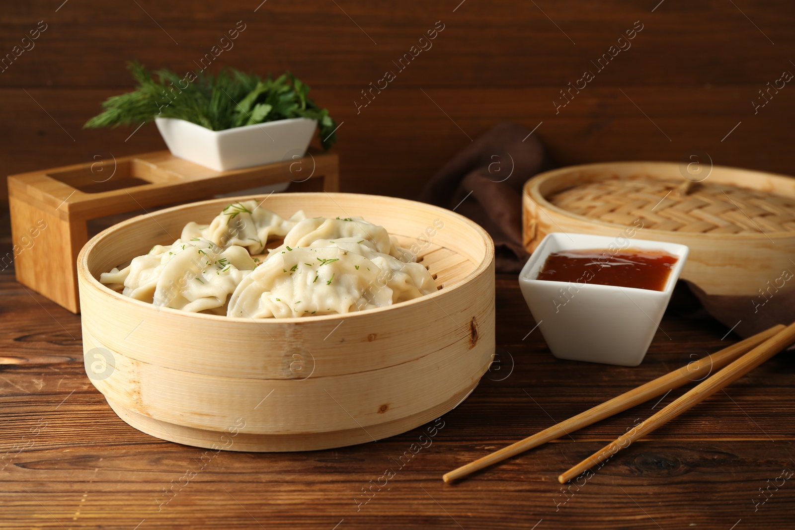 Photo of Tasty boiled gyoza (dumplings) in bamboo steamer, sauce and chopsticks on wooden table