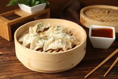 Photo of Tasty boiled gyoza (dumplings) in bamboo steamer, sauce and chopsticks on wooden table, closeup