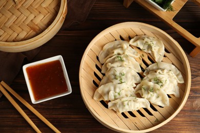 Photo of Tasty boiled gyoza (dumplings) in bamboo steamer, sauce and chopsticks on wooden table, flat lay