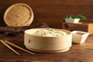 Photo of Tasty boiled gyoza (dumplings) in bamboo steamer, sauce and chopsticks on wooden table