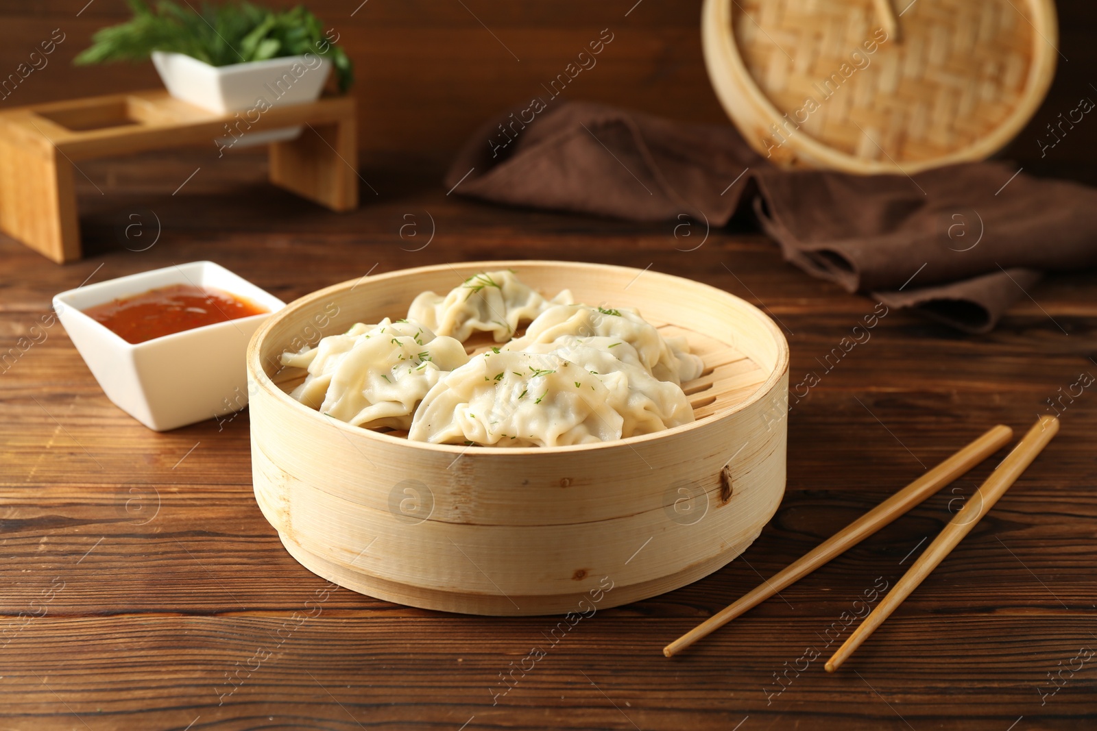 Photo of Tasty boiled gyoza (dumplings) in bamboo steamer, sauce and chopsticks on wooden table