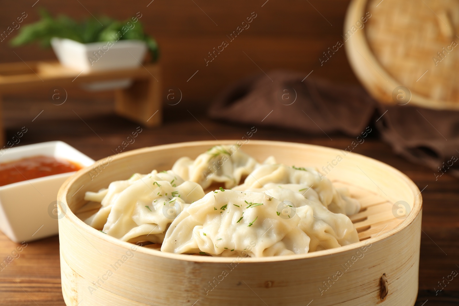 Photo of Tasty boiled gyoza (dumplings) in bamboo steamer and sauce on wooden table, closeup