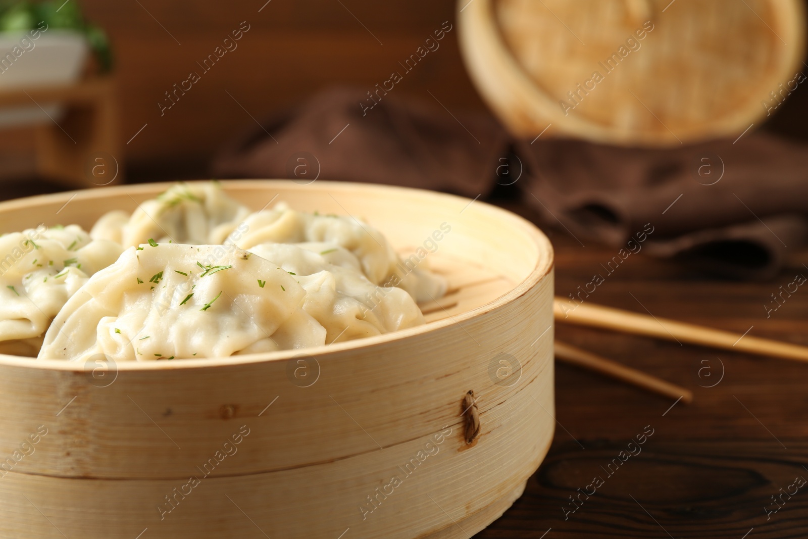 Photo of Tasty boiled gyoza (dumplings) in bamboo steamer and chopsticks on wooden table, closeup