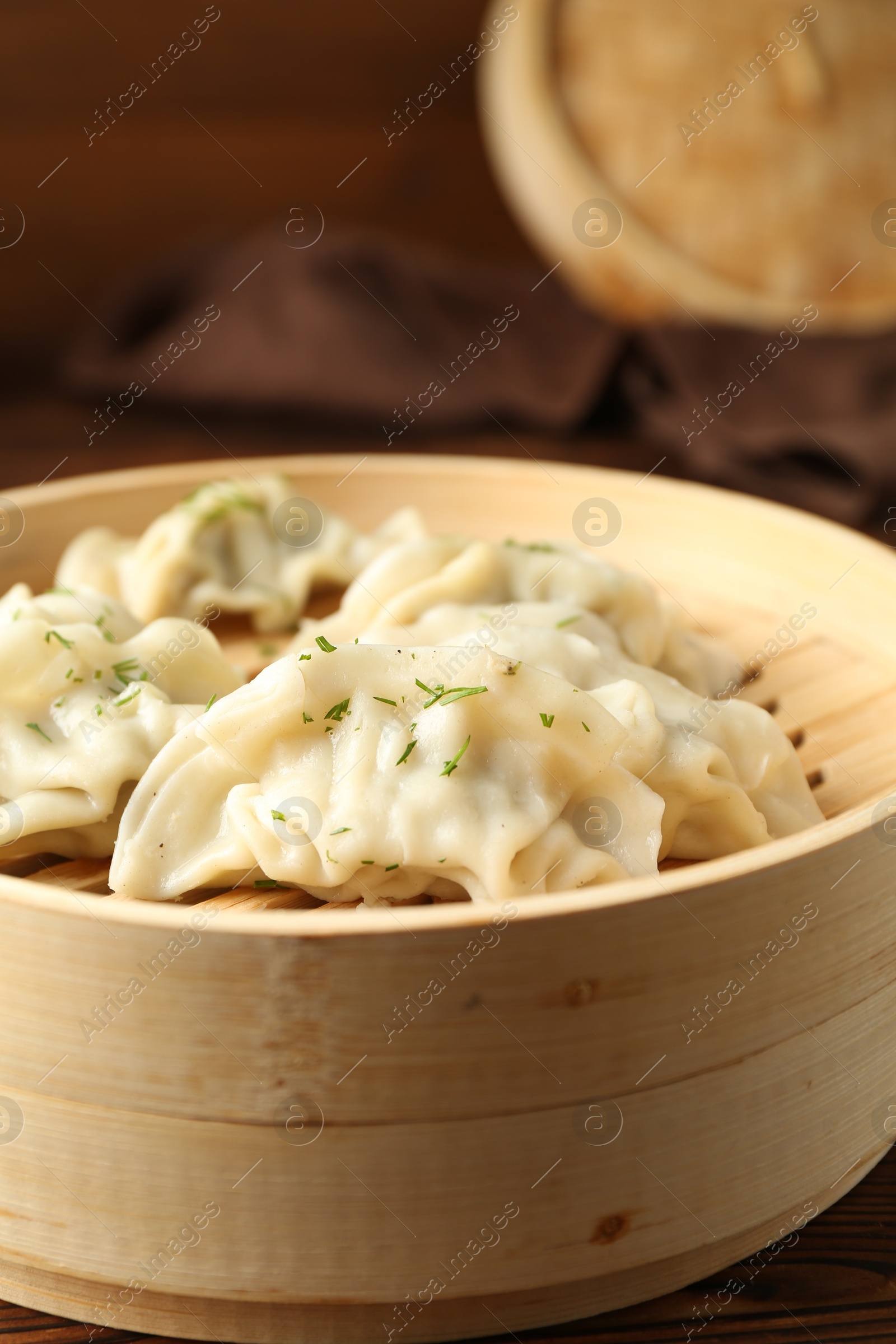 Photo of Tasty boiled gyoza (dumplings) in bamboo steamer on wooden table, closeup