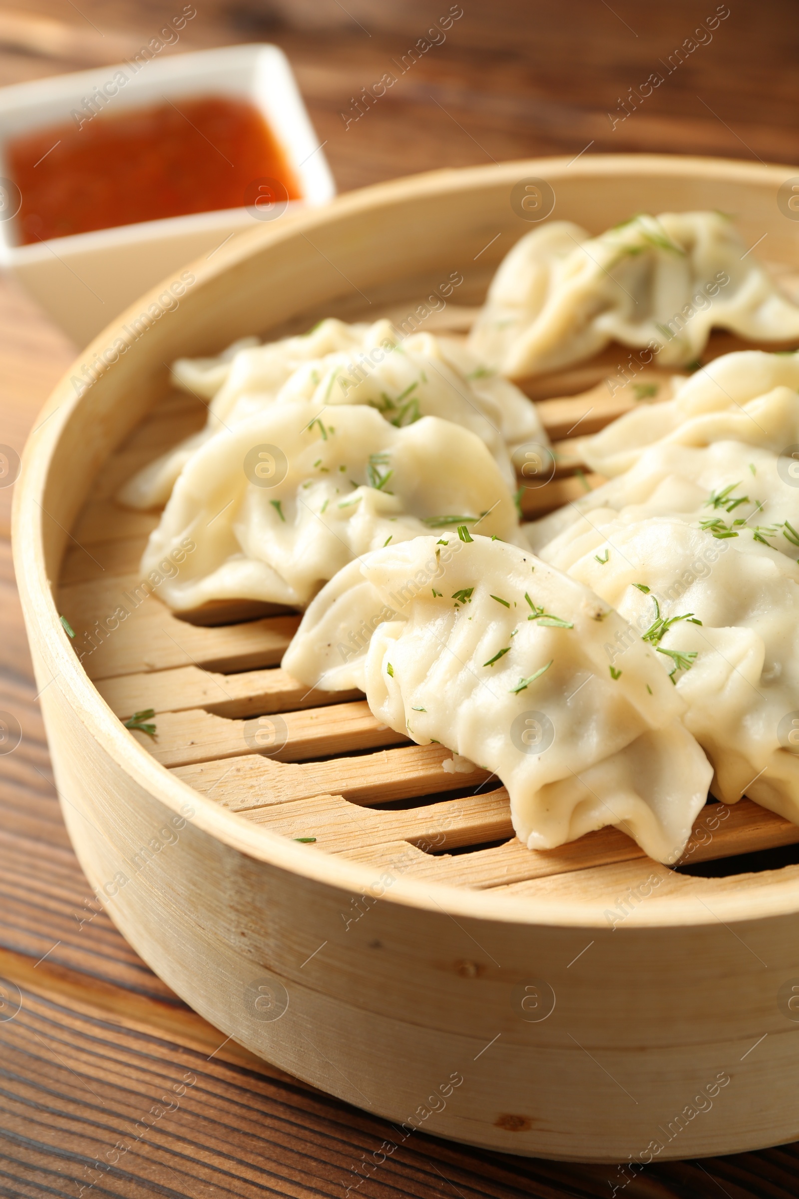 Photo of Tasty boiled gyoza (dumplings) in bamboo steamer on wooden table, closeup