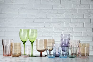 Photo of Many different glasses on white marble table against brick wall. Space for text