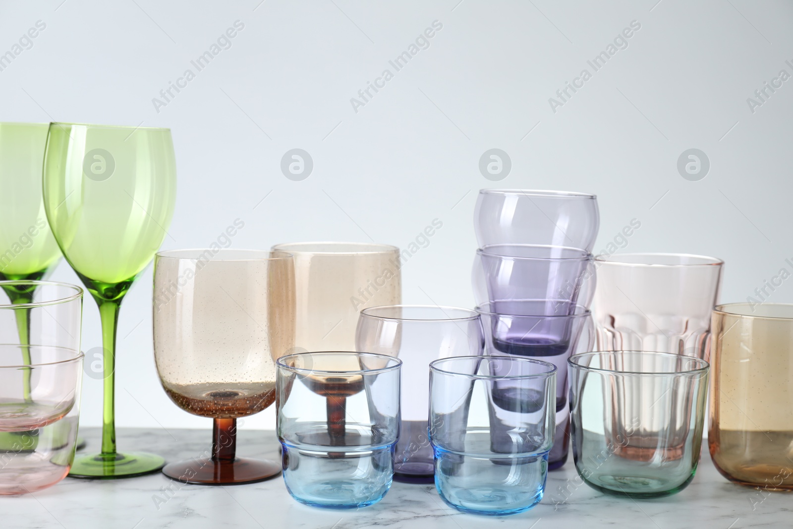 Photo of Many different glasses on white marble table against light background