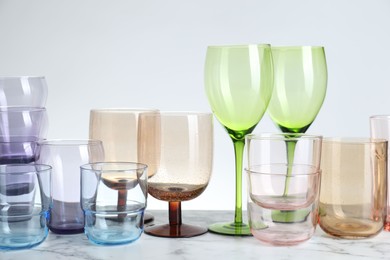 Photo of Many different glasses on white marble table against light background