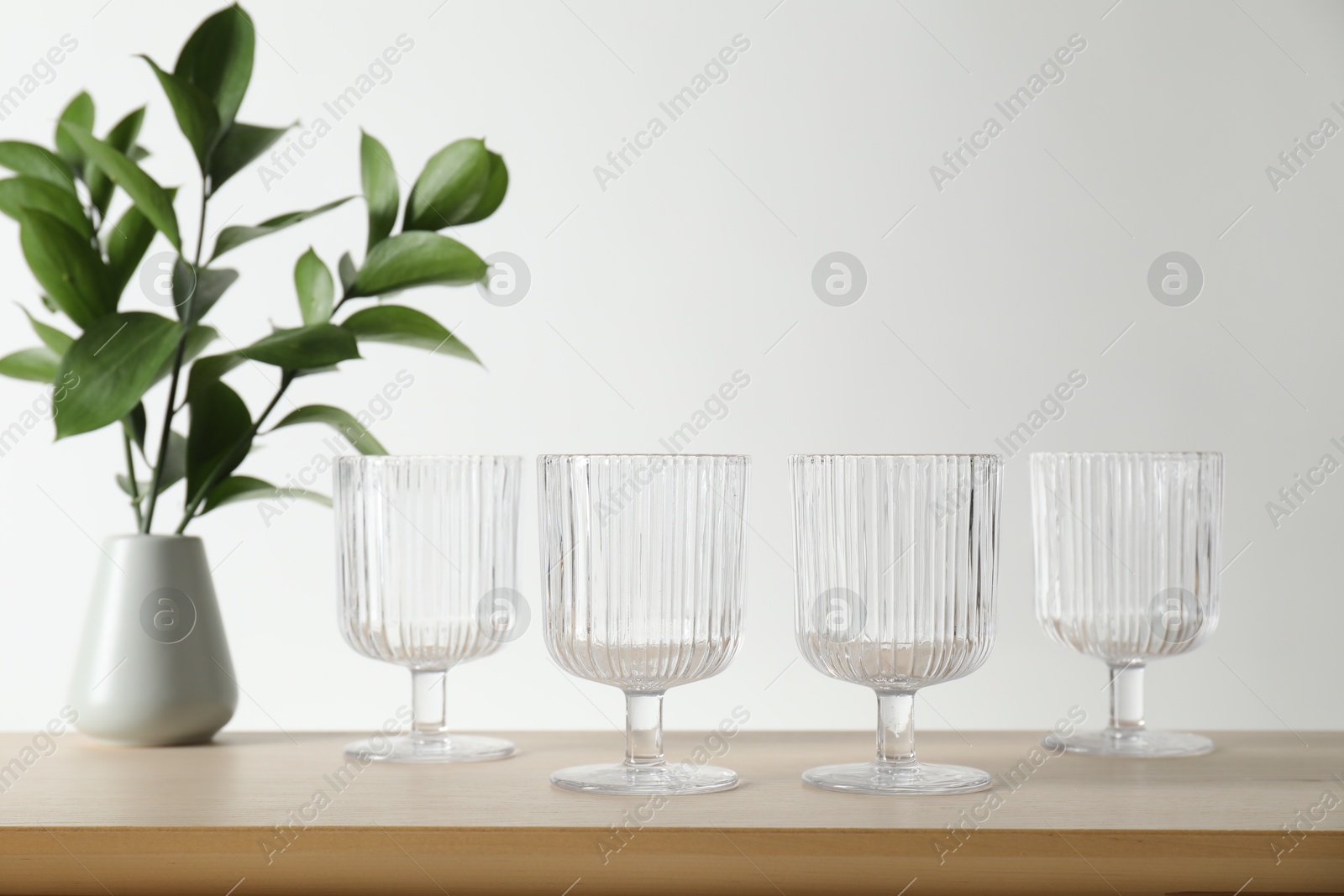 Photo of Many empty clean glasses and vase with leaves on wooden table. Space for text