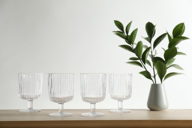 Photo of Many empty clean glasses and vase with leaves on wooden table. Space for text